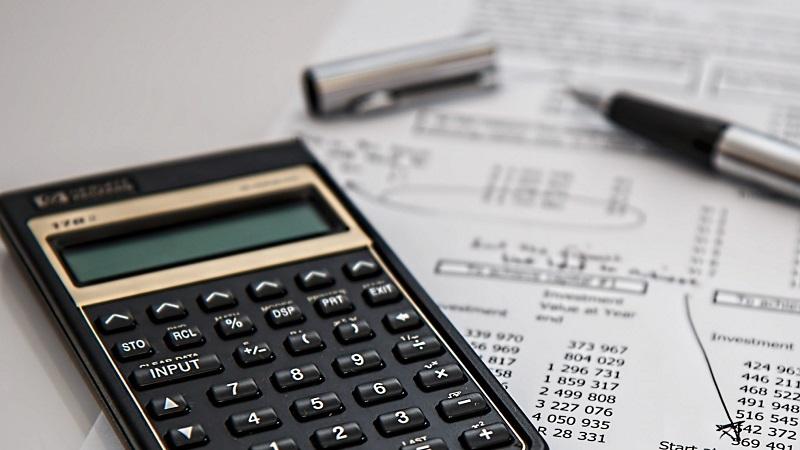 An image of a calculator, and a fountain pen lying on top of a piece of paper with accounting information