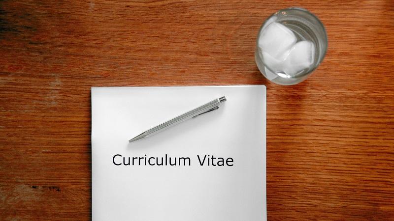 An image of a document labelled &#039;Curriculum vitae&#039; lying on a table next to a glass of water