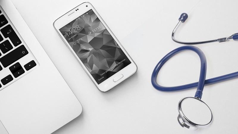 An image of the edge of a laptop next to a smartphone and stethoscope