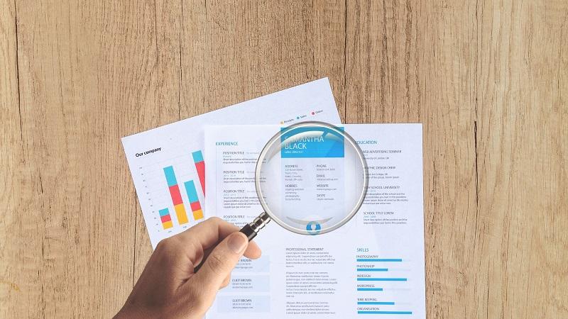 An image of a magnifying glass hovering over a CV and company documents