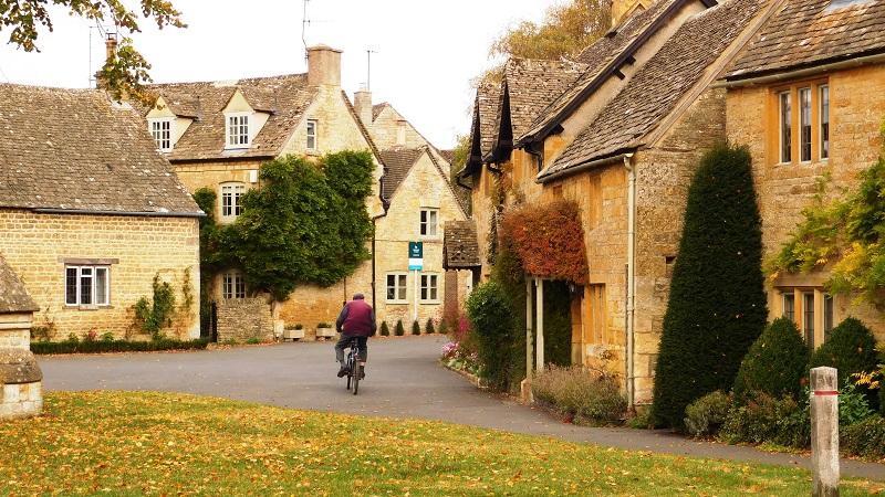 An image of someone riding a bicycle through a village in the Cotswolds