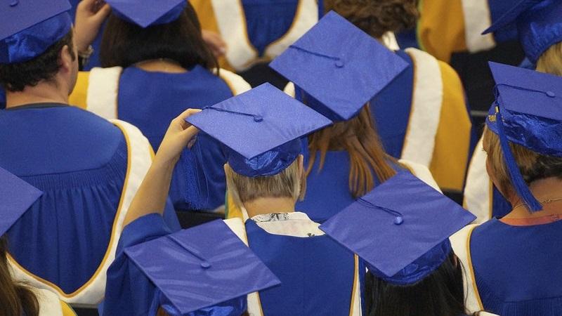 An image of university graduates, pictured from behind and wearing mortar boards and gowns