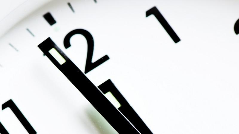 A close-up image of a clock with the hands approaching 12 o&#039;clock