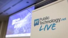 A close-up image of a lectern and a screen in the background, displaying the PublicTechnology Live logo