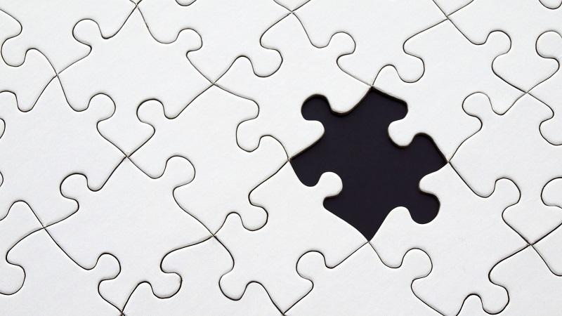A close-up image of a plain puzzle with one piece missing from the middle