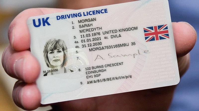 A close-up image of a hand holding an example UK driving licence