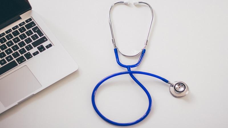 An image of a stethoscope lying next to a laptop computer