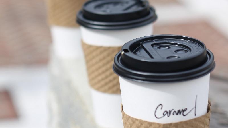 A close-up image of three takeaway coffee cups, with &#039;Caramel&#039; written on the closest one