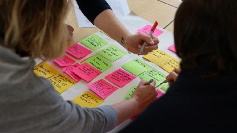 An image of user researchers working on a document with various sticky notes
