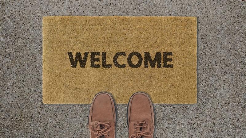 An image of a welcome mat with two shoes perched on the edge