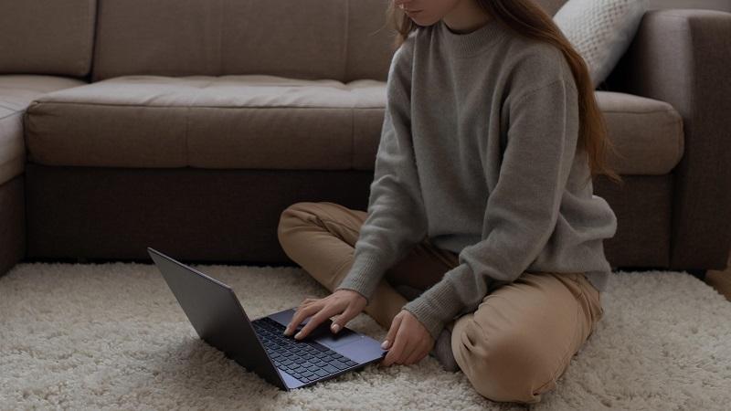An image of a young woman sitting on the floor looking at a laptop