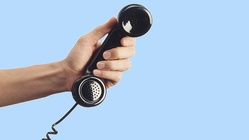 An image of a hand holding a landline phone handset, on a blue background